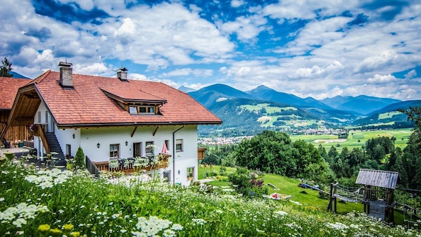 A white building with a red roof, a wooden staircase, and a view of a valley with mountains in the background. - Apartment 'Kranebitterhof Alpenrose' with Mountain View, Shared Garden and Wi-Fi (Valdaora)