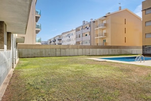 Um edifício residencial com piscina, muro de concreto e gramado.