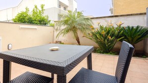 Un patio con mesa y sillas, rodeado de plantas y un edificio.