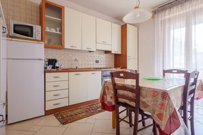 Una cocina con armarios blancos, microondas, cafetera y una mesa de comedor con sillas.