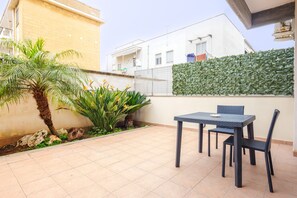 Un patio con una mesa, sillas, una palmera y un seto.