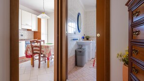 Un umbral abierto que da a una cocina con mesa, sillas y un cubo de basura.