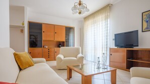 Una sala de estar con un sofá, sillones, una mesa de centro, un televisor y un aparador de madera.