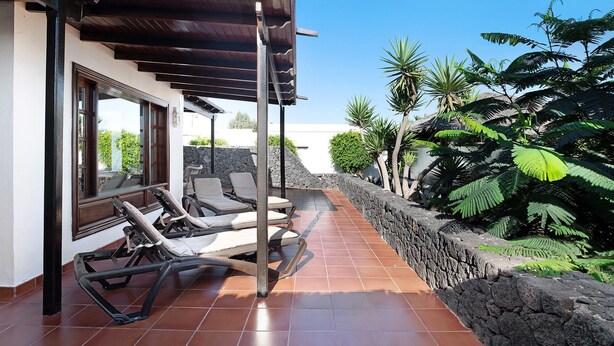 A covered outdoor area with lounge chairs, a stone wall, and tropical plants.