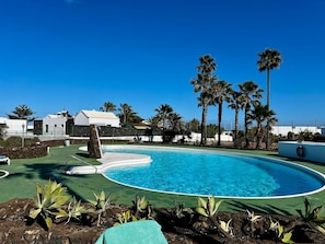 Une piscine à bordures courbes, entourée de palmiers et d’un mur de pierre.