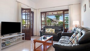 A living room with a TV, a leather sofa, a coffee table, and a bookshelf.
