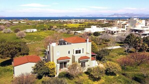 A residential area with houses, green fields, and a distant view of the sea and mountains.