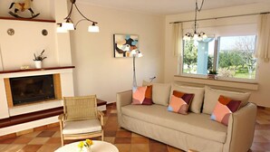 A living room with a sofa, chairs, a fireplace, a window with a view, and a floor with patterned tiles.
