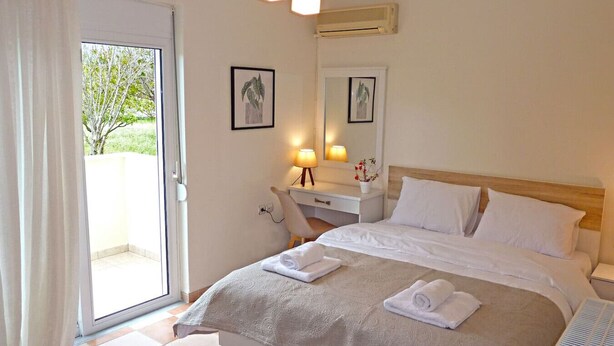 A hotel room with a bed, a desk, a chair, a mirror, and a window with a view of trees.