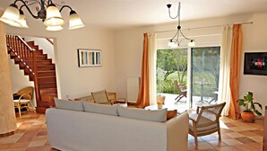 A living room with a sofa, chairs, a staircase, and a view through a large window.