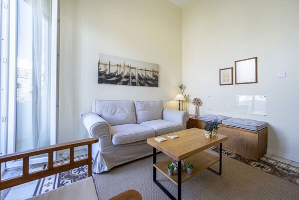 A living room with a sofa, a wooden coffee table, a small plant, and a painting on the wall.