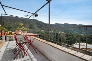 Un balcón con una mesa y sillas, plantas en macetas y vistas a un paisaje montañoso.