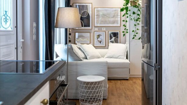 Una cocina compacta con refrigerador, una zona de comedor con mesa y sillas, y un pequeño rincón de estar con sofá y lámpara.