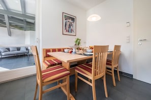 A dining area with a wooden table and chairs, a bench, a vase with flowers, and a painting on the wall.
