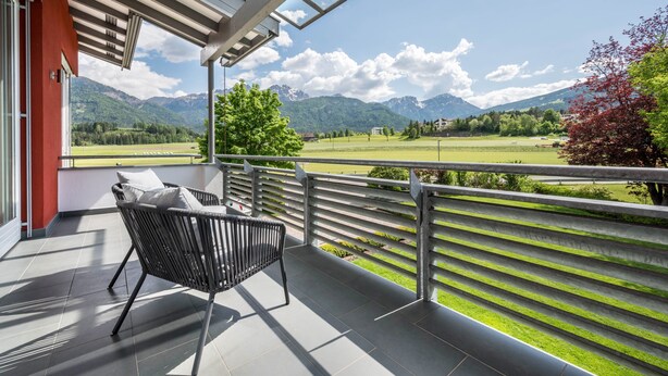 A balcony with a chair, a view of a green field, and mountains in the background. - Apartment 'Suite Marianne' with Mountain View, Private Terrace and Wi-Fi (Valdaora)