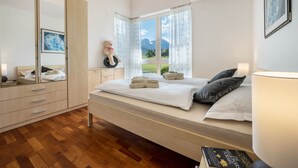 A bedroom with a bed, a dresser, a mirror, a window with a view of mountains, and a lamp. - Apartment 'Suite Marianne' with Mountain View, Private Terrace and Wi-Fi (Valdaora)
