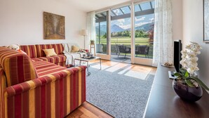 A living room with a striped sofa, a coffee table, a TV, and a potted plant. - Apartment 'Suite Marianne' with Mountain View, Private Terrace and Wi-Fi (Valdaora)