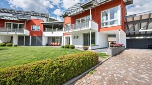 A modern two-story house with a red facade, large windows, and a well-maintained lawn. - Apartment 'Suite Marianne' with Mountain View, Private Terrace and Wi-Fi (Valdaora)