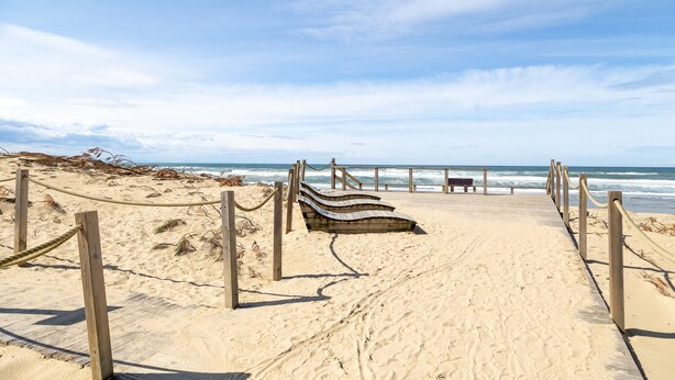 Ein sandiger Strand mit Holzboden und einer Bank.