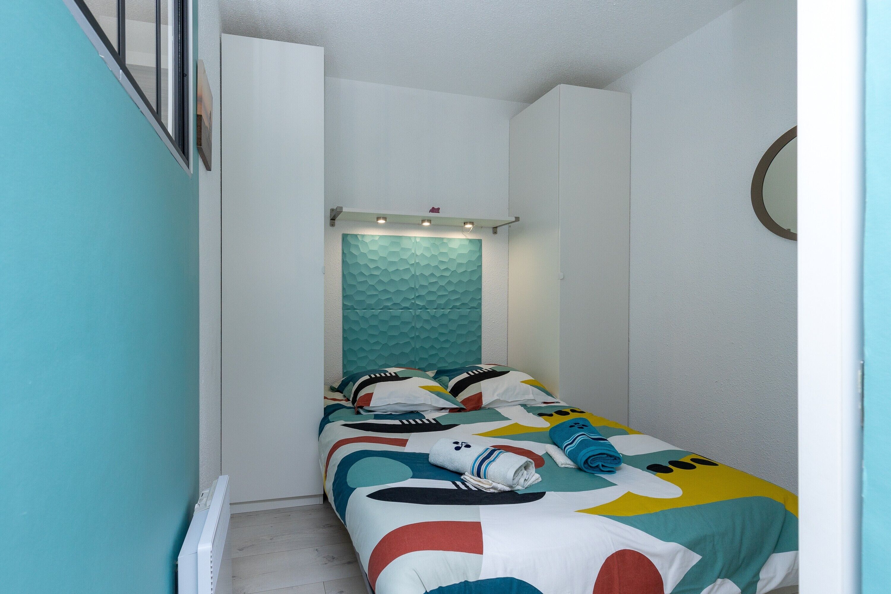 A narrow room with a bed, a window, and a wall-mounted shelf.
