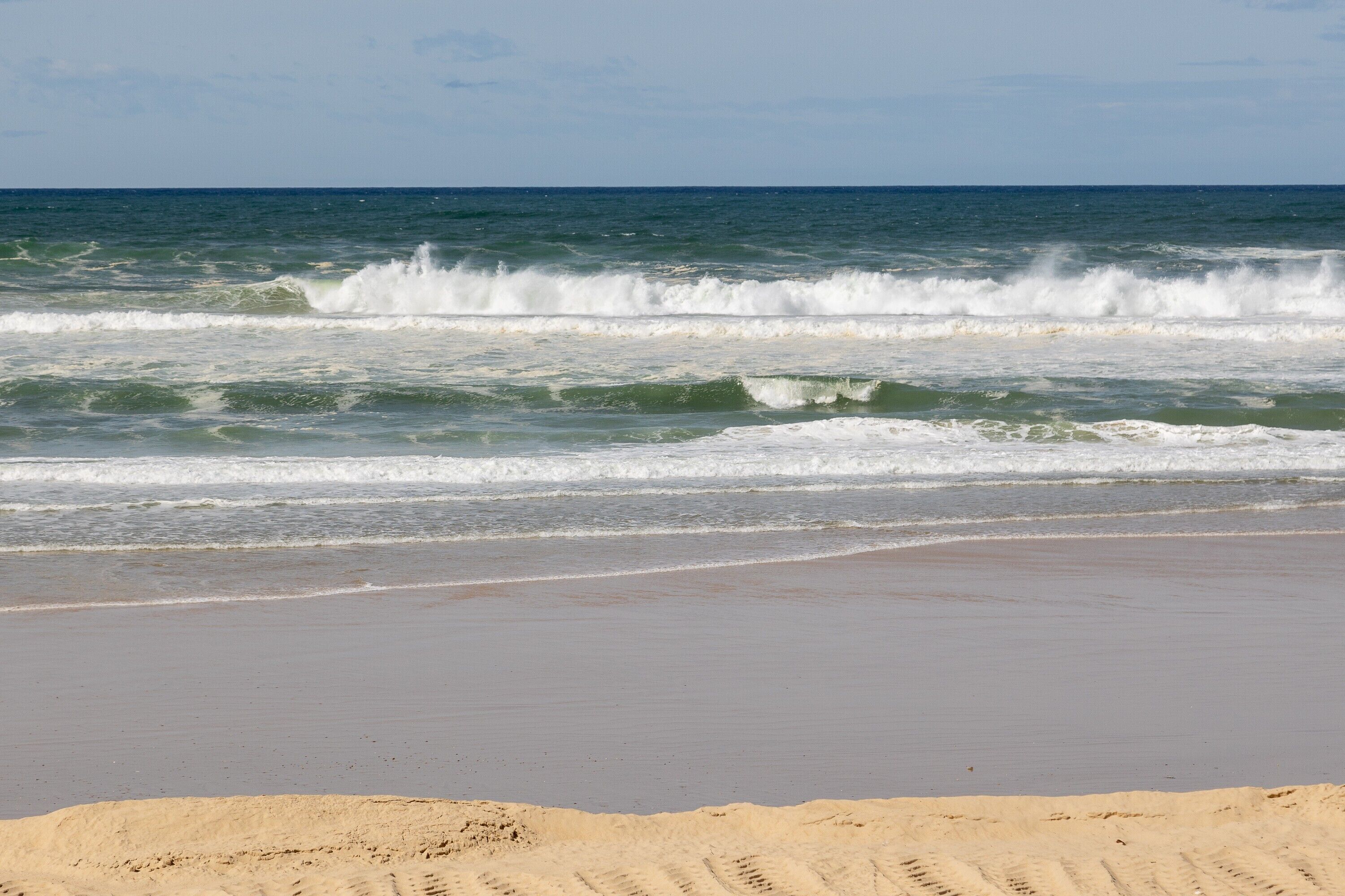 A beach with waves, a sandy shore, and a clear sky.