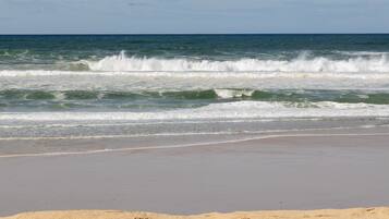 A beach with waves, a sandy shore, and a clear sky.