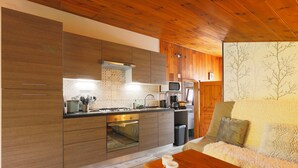 A modern kitchen with wooden cabinets, a microwave, and a dining area with a table and sofa. - Le Chalet Cosy - Label Valeurs Parc Naturel Régional (Weiterswiller)