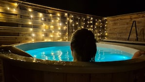 Una persona en un jacuzzi con un muro de madera y luces colgantes.