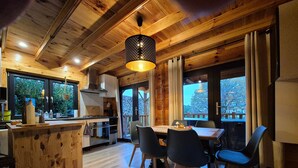 Een houten interieur met een keuken en eethoek, grote ramen en een hanglamp.