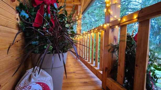 Een houten terras met een leuning, versierd met lichtslingers en een kerstkrans.