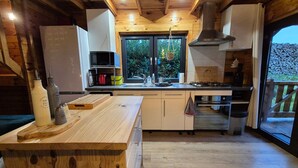 Een keuken met houten kasten, een centraal eiland, een fornuis en een raam met uitzicht op groen.