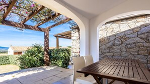 A patio with a wooden table and chairs, stone walls, and a view of the countryside. - Holiday Home 'Casa Gio' with Sea View, Garden, Shared Pool and Wi-Fi (Badesi)