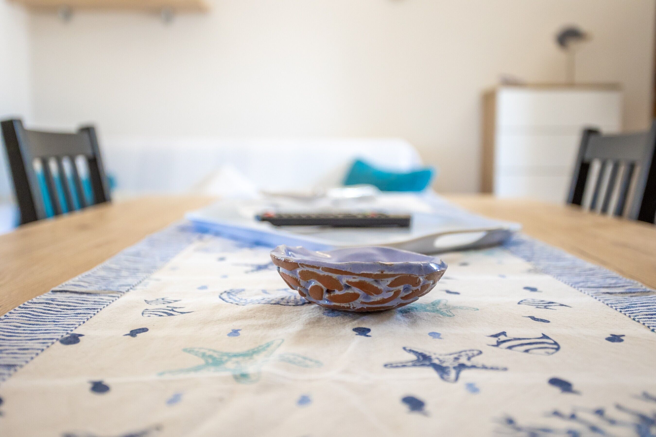 Una mesa de comedor con un mantel estampado, un cuenco decorativo y un control remoto.