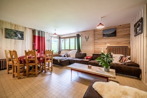 Ein Zimmer mit Holzwänden, einem Esstisch, Stühlen, einer Couch und einem Couchtisch.