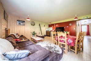 Ein gemütliches Zimmer mit einer Couch, einem Esstisch mit Stühlen, einer Uhr an der Wand und Holzboden.