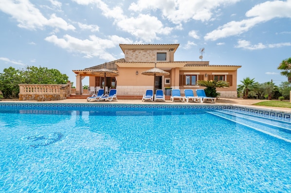 A swimming pool with lounge chairs, a building with a tiled roof, and a clear sky.