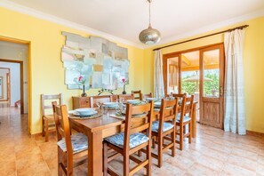 A dining area with a wooden table set for six, chairs with cushioned seats, a wall art piece, and a view through a glass door.