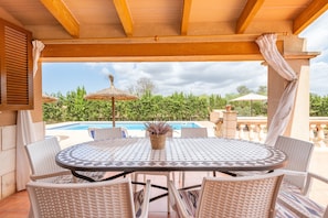 A covered outdoor seating area with a pool view, wicker furniture, and a thatched umbrella.