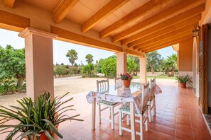 An outdoor patio with a glass table and chairs, surrounded by potted plants and a view of the garden.