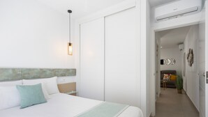 Ein Schlafzimmer mit Bett, Nachttisch, Lampe und Blick in einen anderen Raum.