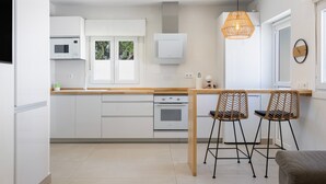 Eine moderne Küche mit weißen Schränken, einer Holz Arbeitsplatte und zwei Korbstühlen.