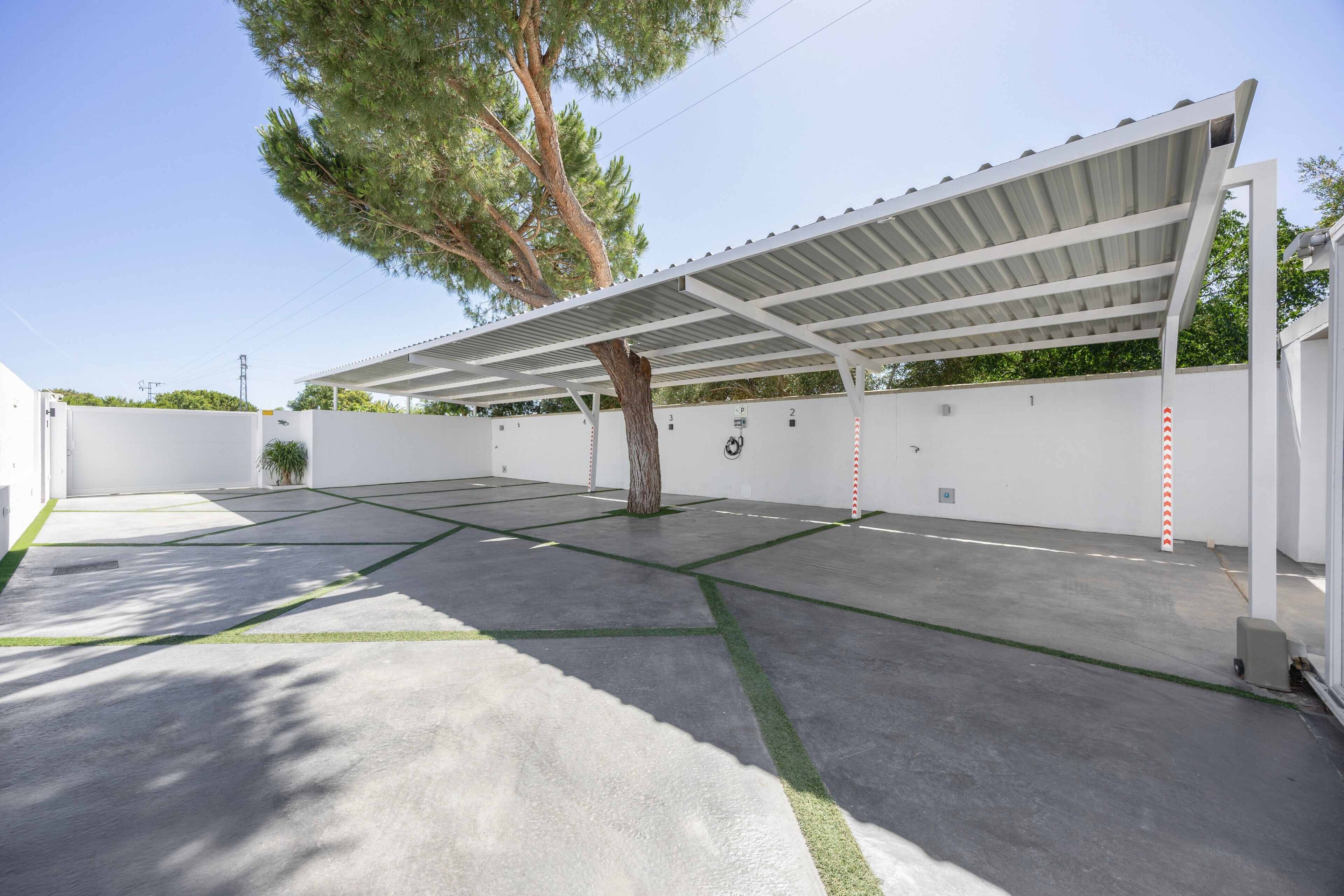 A covered parking area with a tree, white walls, and a clear sky.