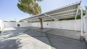 A covered parking area with a tree, white walls, and a clear sky.