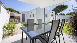 Eine Terrasse im Freien mit einem Glastisch und Stühlen, einem Pool und einem weißen Haus im Hintergrund.