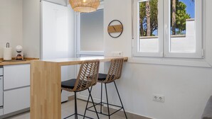 Eine moderne Küche mit einer Holzinsel, zwei Barhocker, einer Hängelampe und einem Fenster mit Blick auf Bäume.