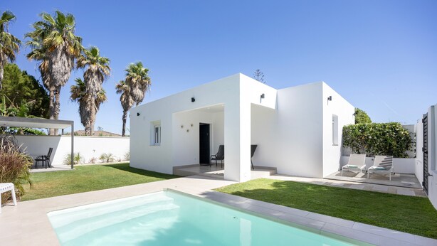 Ein modernes Haus mit Swimmingpool, heller Fassade und Palmen.