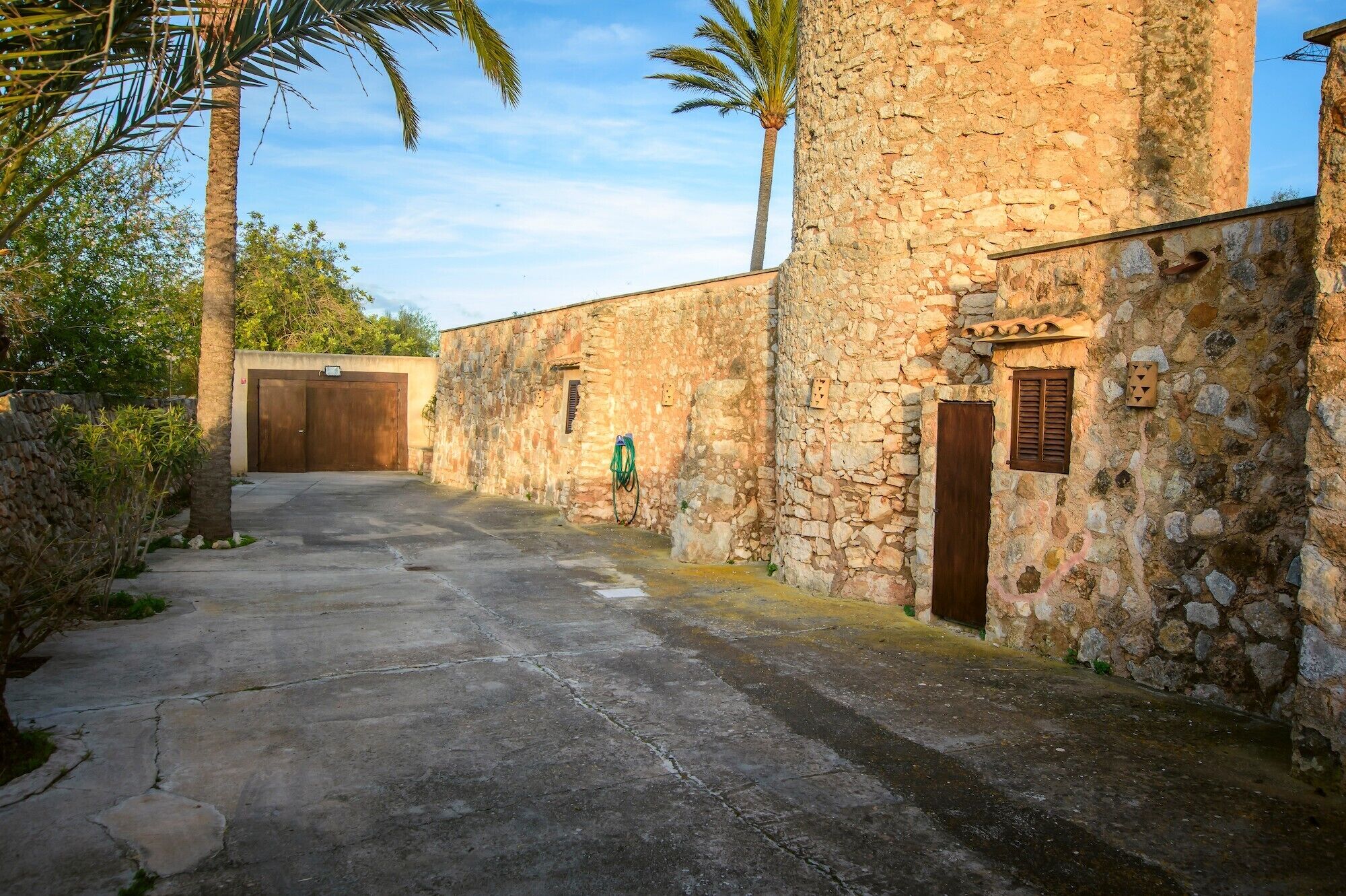 A stone building with a concrete pathway, a wooden door, and a small window with shutters.