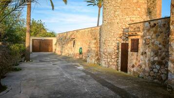 A stone building with a concrete pathway, a wooden door, and a small window with shutters.
