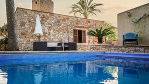Ein Gebäude aus Stein mit Pool, Sitzgelegenheiten im Freien und einer Palme.