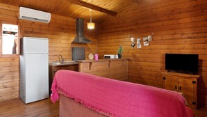 A wooden cabin interior with a kitchenette, a refrigerator, a sink, a microwave, a stove, a television, and a pink blanket on a bench. - Holiday Home "Casa Juana Madera" with Shared Pool and Air Conditioning (Zahora)